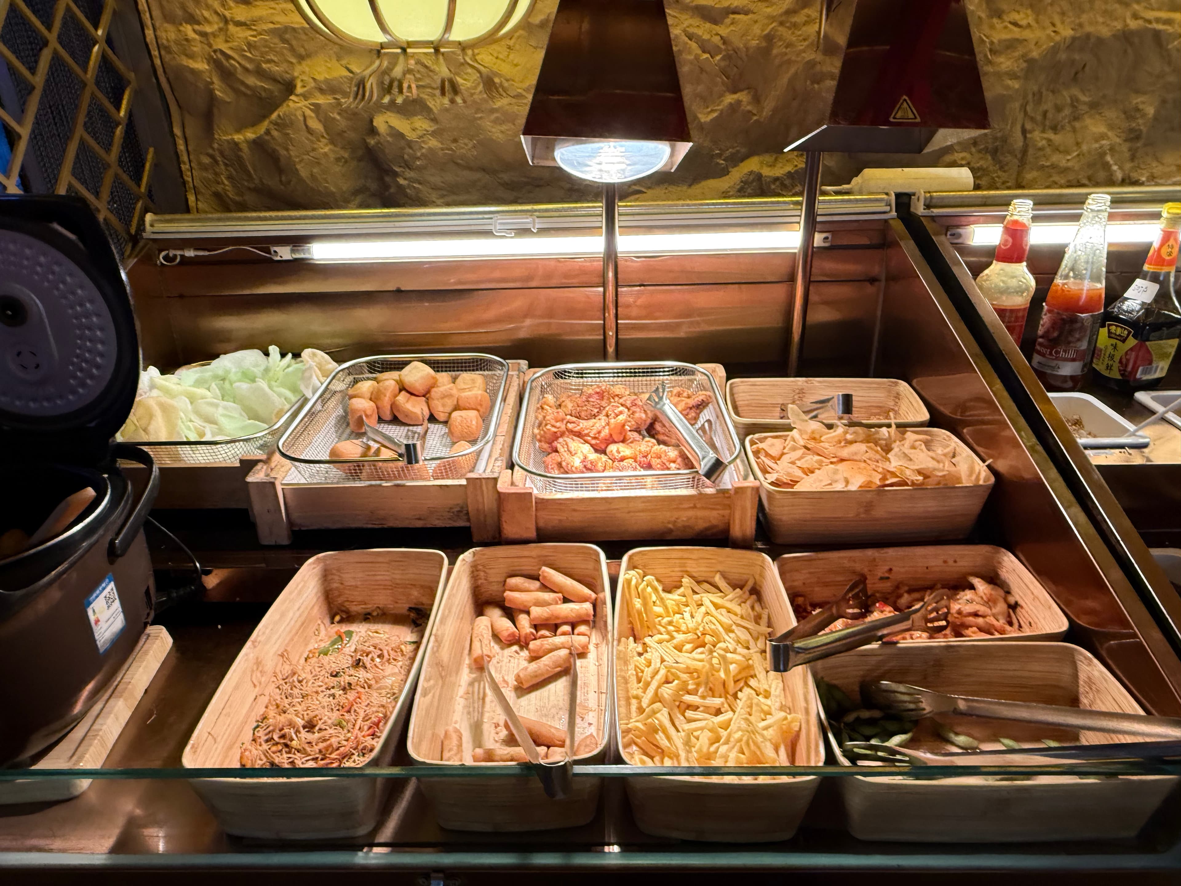 Cooked side dishes at the Sukijoy buffet including noodles, spring rolls, and chicken wings